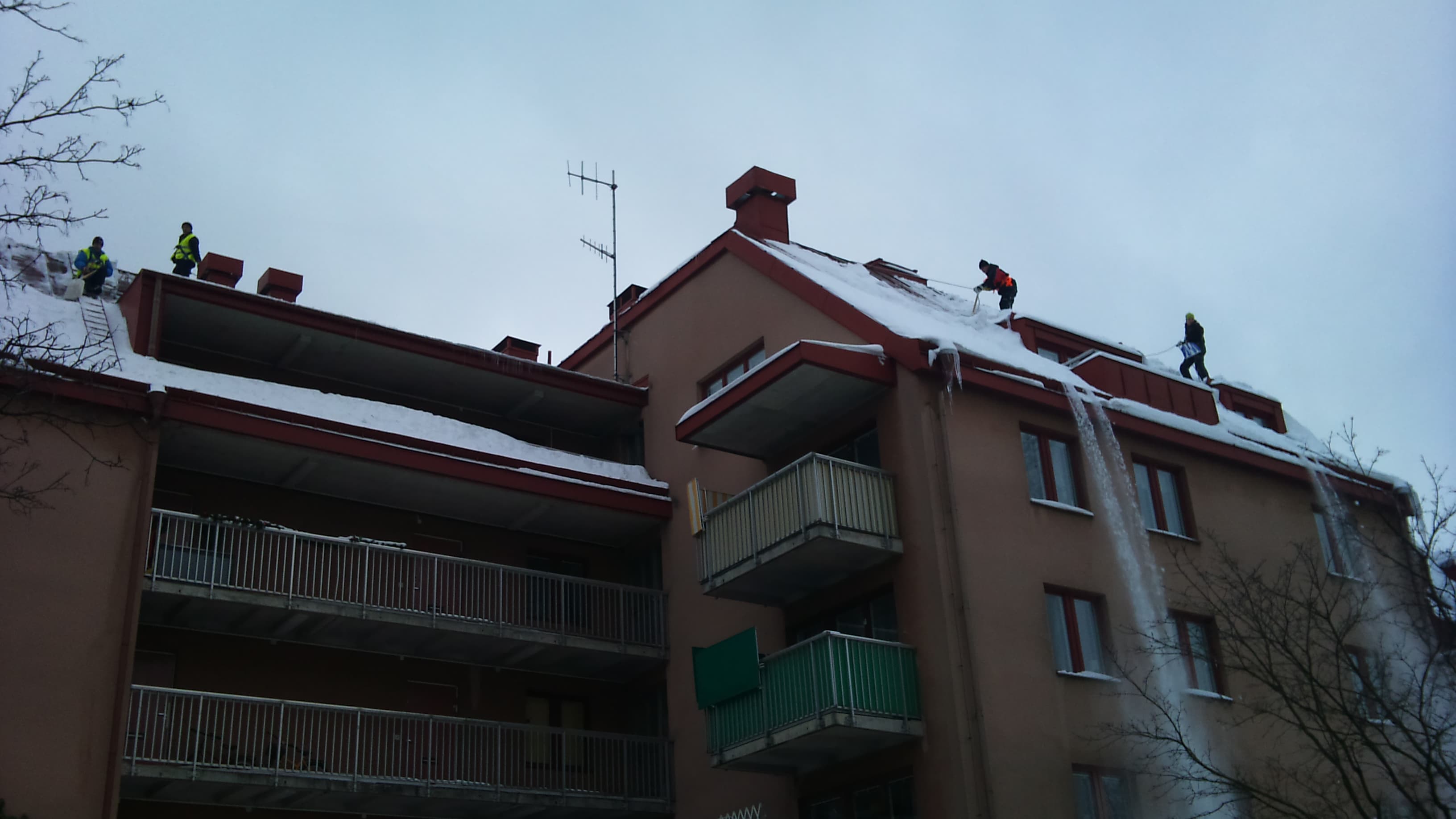 Personer arbetar med snöskottning på ett flerbostadshus med balkonger.