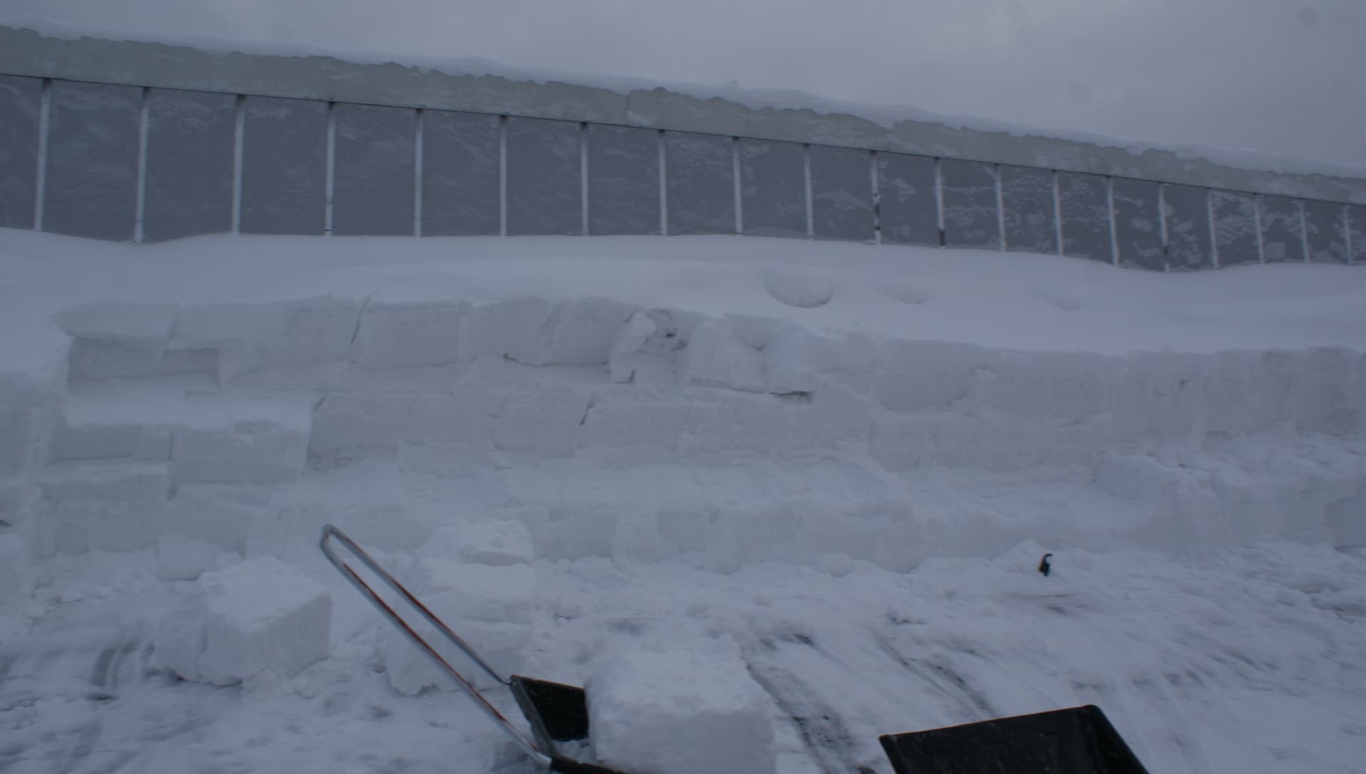 Djupa snölager och en skottad yta på taket, med snöredskap i förgrunden.
